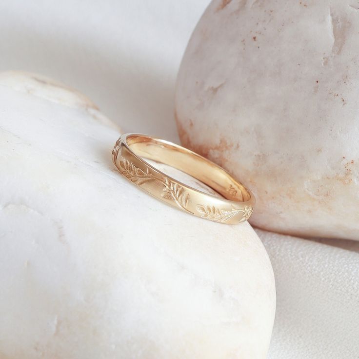 a gold wedding ring sitting on top of a white marble surface next to a rock