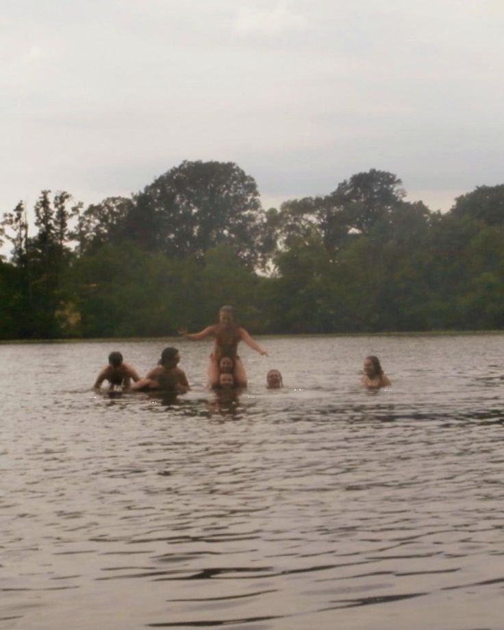 a group of people in the water playing frisbee with trees in the background