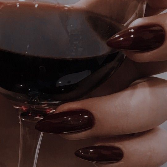 a woman's hand holding a wine glass with dark colored nail polish on it