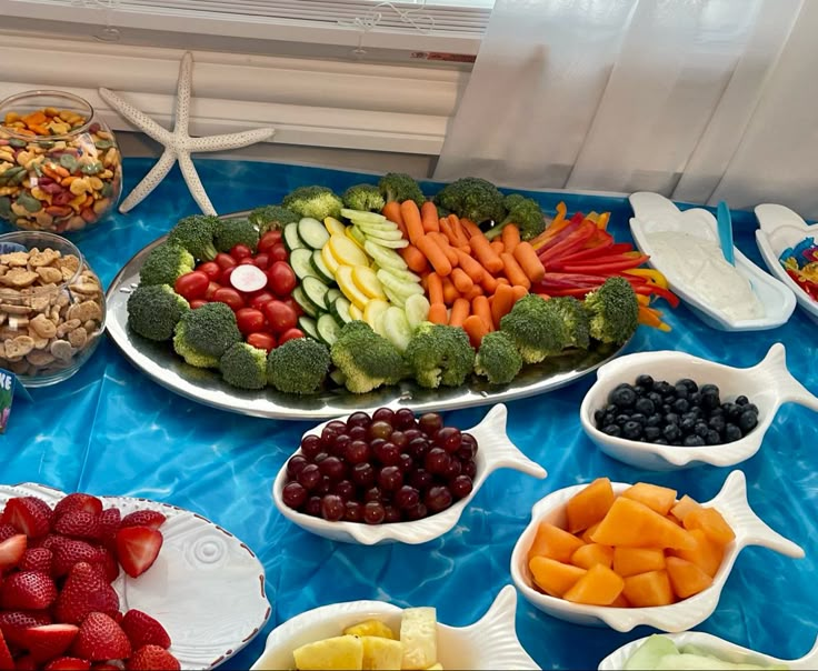 an assortment of fruits and vegetables on a blue table cloth next to bowls of fruit