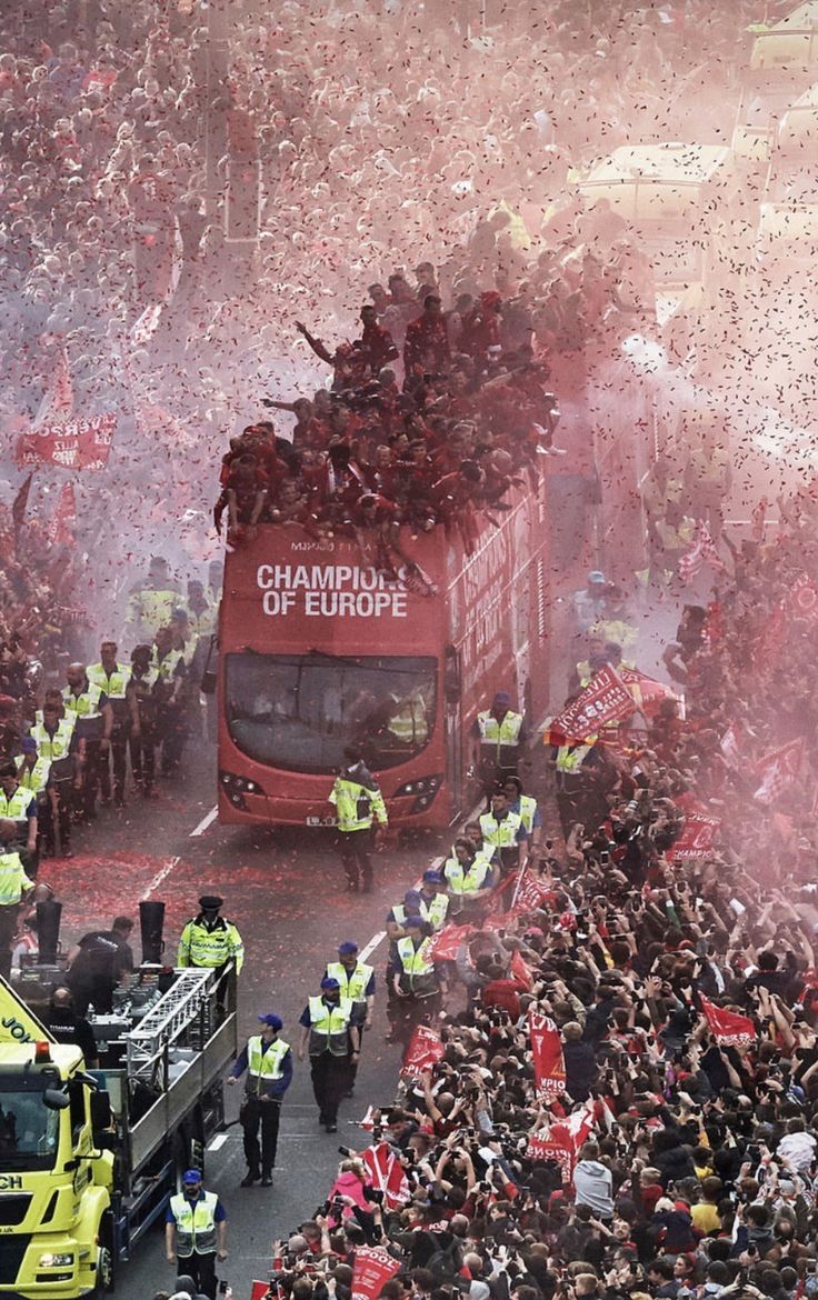 a large group of people standing on top of a red double decker bus driving down a street