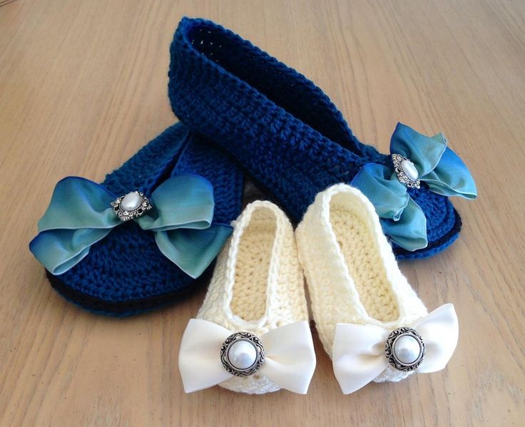 two baby shoes with bows on them sitting on a wooden floor next to a pair of slippers