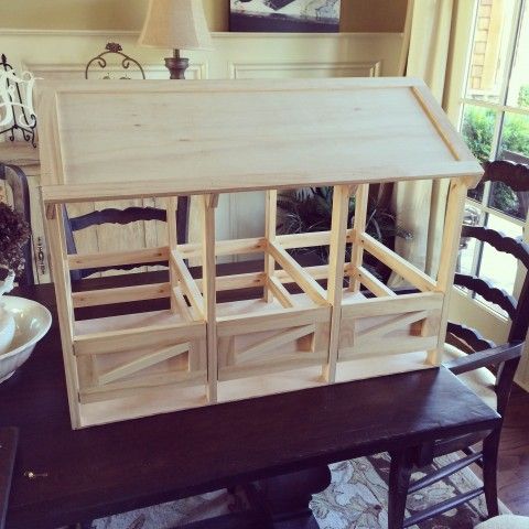 a doll house made out of wood sitting on top of a wooden bench in front of a window