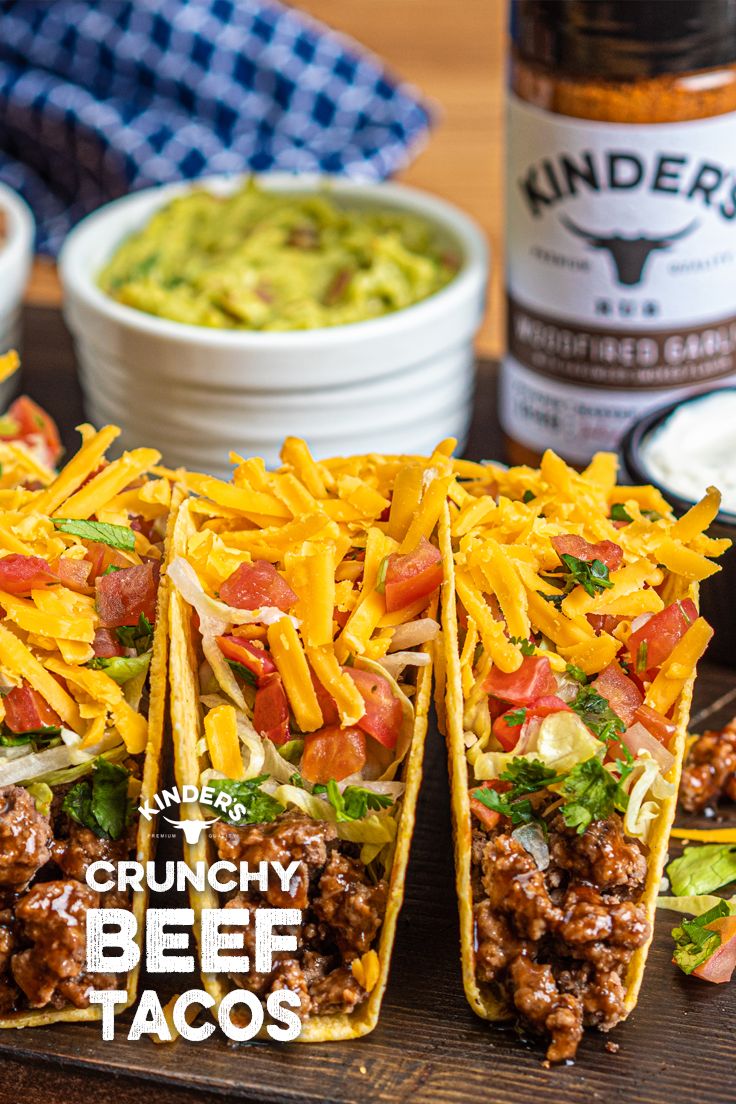 three tacos on a cutting board with condiments and beer in the background