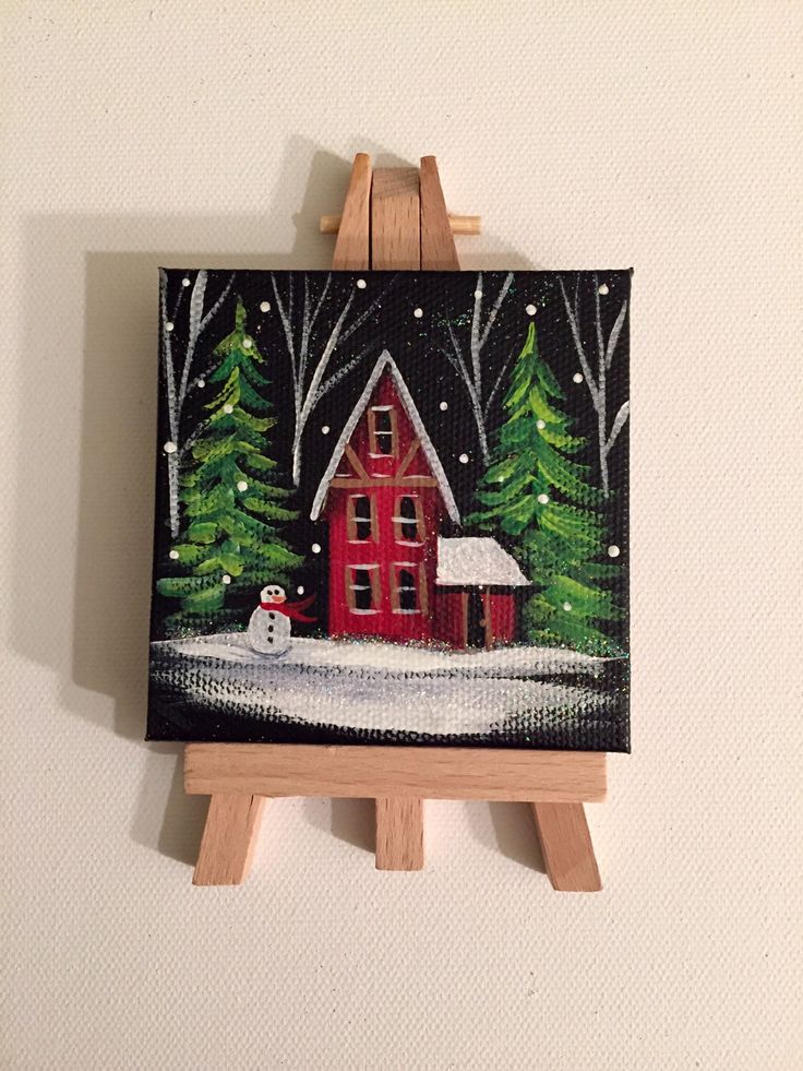 an easel with a painting on it and a red house in the snow next to trees