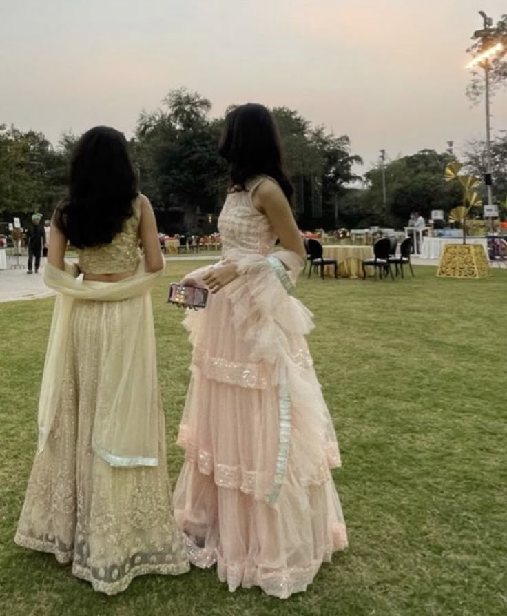 two women in dresses are standing on the grass