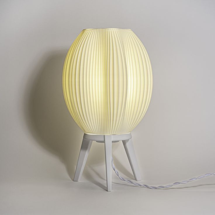 a white lamp sitting on top of a wooden table next to a light bulb and cord