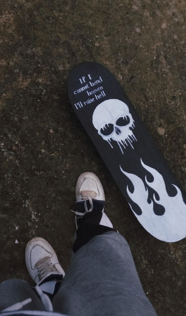 a person standing next to a skateboard with a skull on it's side