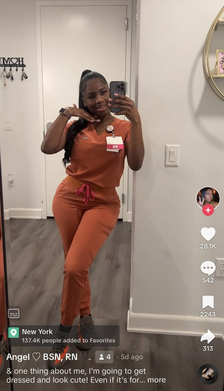 a woman in an orange jumpsuit taking a selfie with her cell phone and smiling