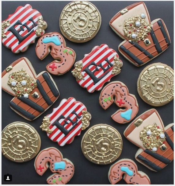 decorated cookies in the shape of pirate ships and chestes are on a black surface