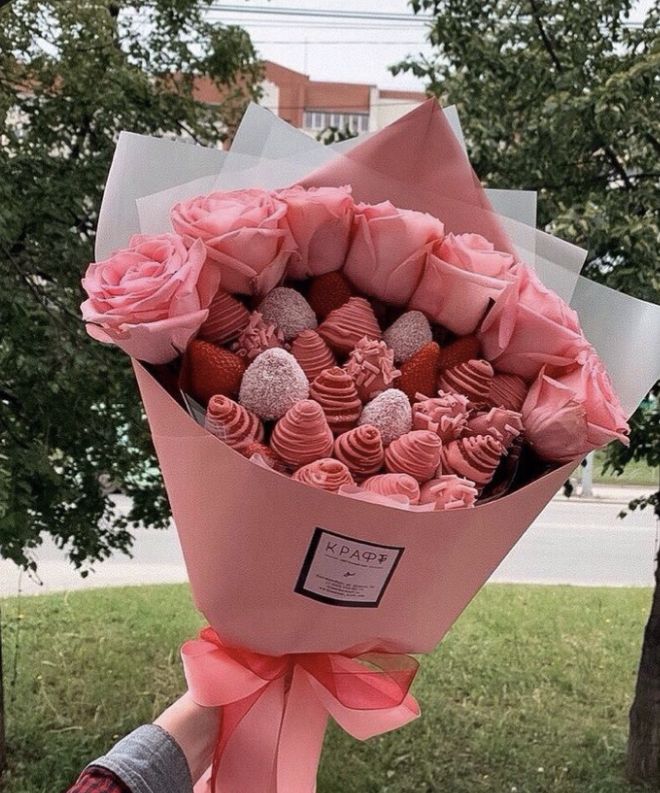 a bouquet of pink roses and chocolates wrapped in paper with a ribbon around it