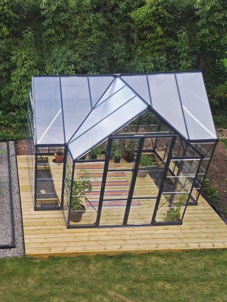 a small glass house sitting on top of a wooden platform in the middle of a yard