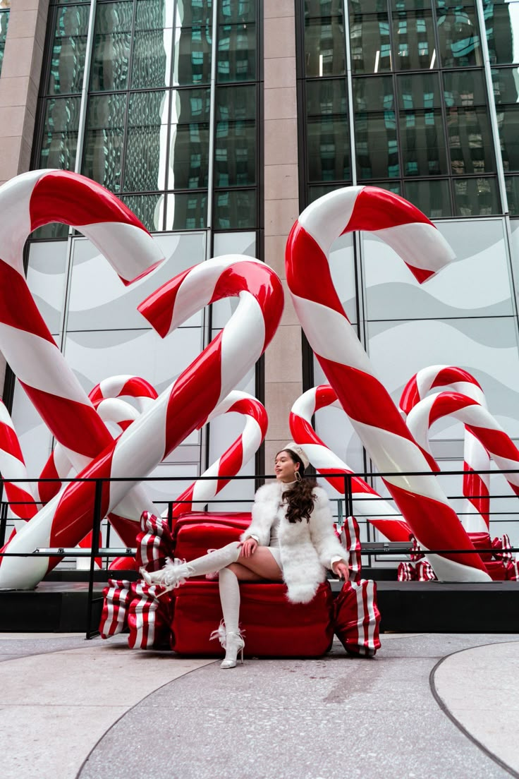 a woman sitting on top of a red suitcase in front of giant candy canes