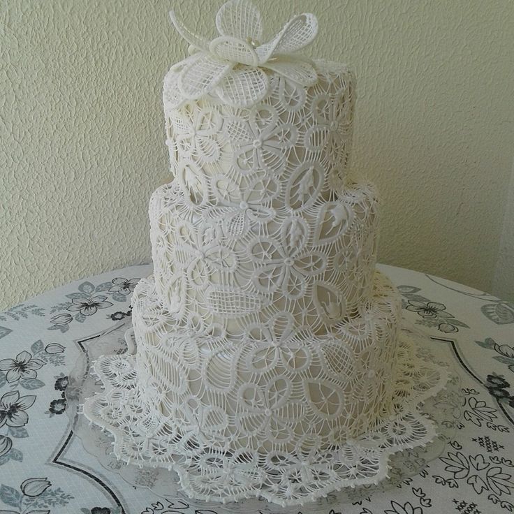 a three tiered white lace cake on top of a doily covered tablecloth