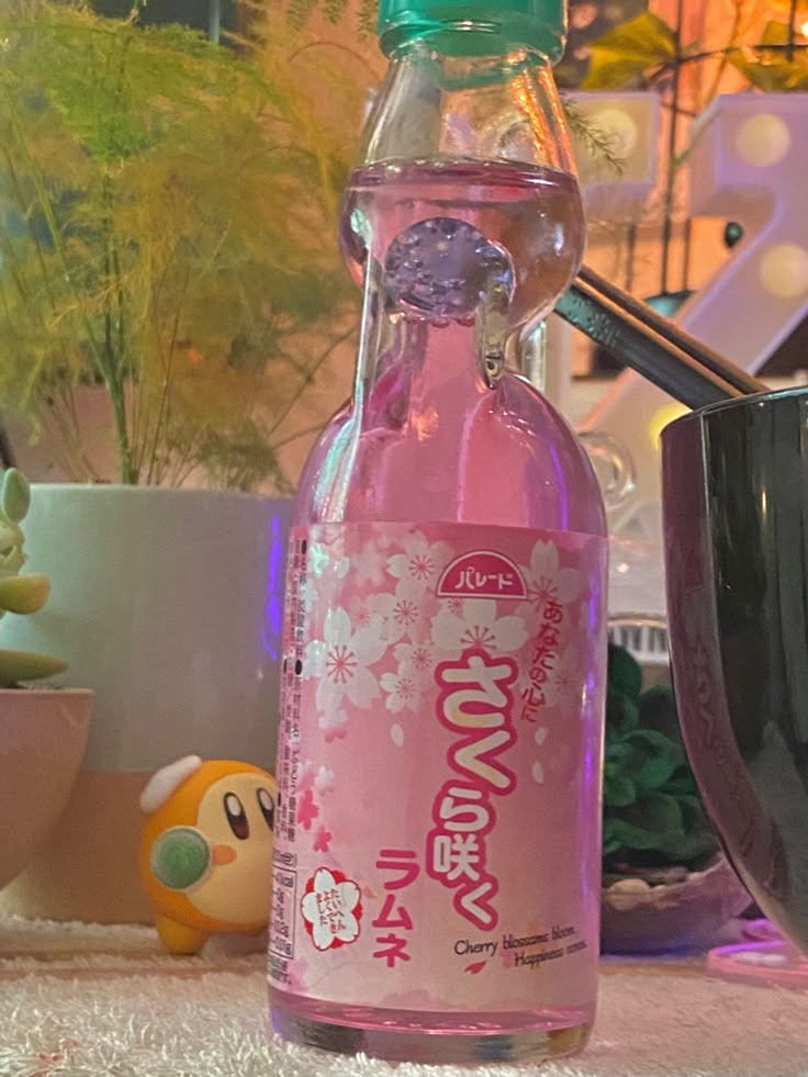 a bottle of pink liquid sitting on top of a table next to a potted plant