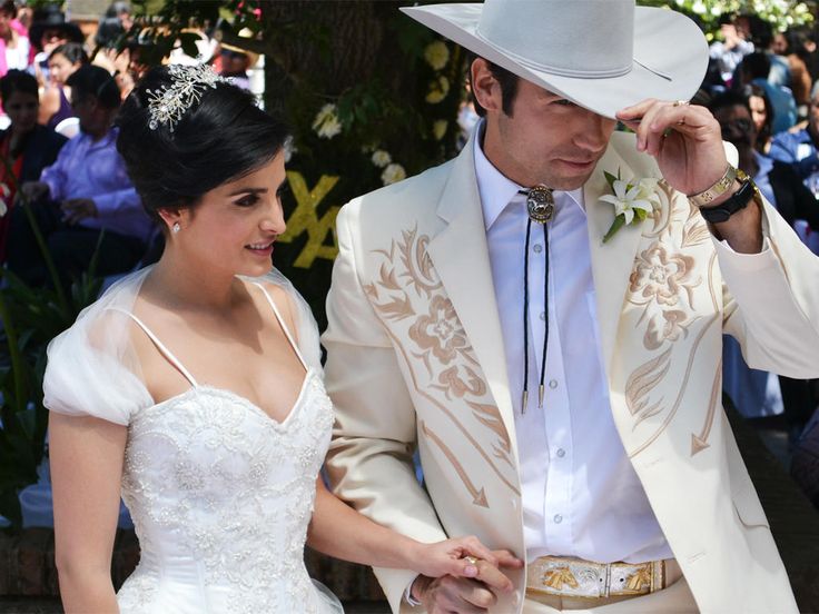 a man in a white suit and hat walking next to a woman wearing a wedding dress