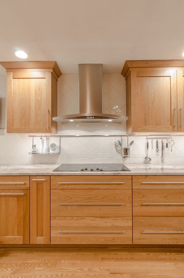 an empty kitchen with wooden cabinets and stainless steel range hood over the sink, in front of white tiled backsplash