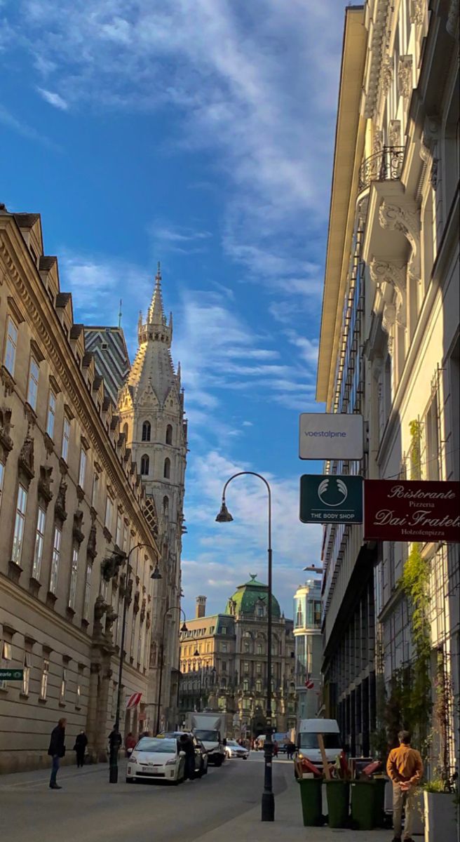 people are walking down the street in an old european city with tall buildings on both sides