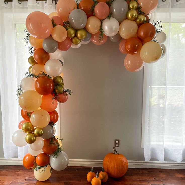 an arch made out of balloons and pumpkins on the floor in front of a window