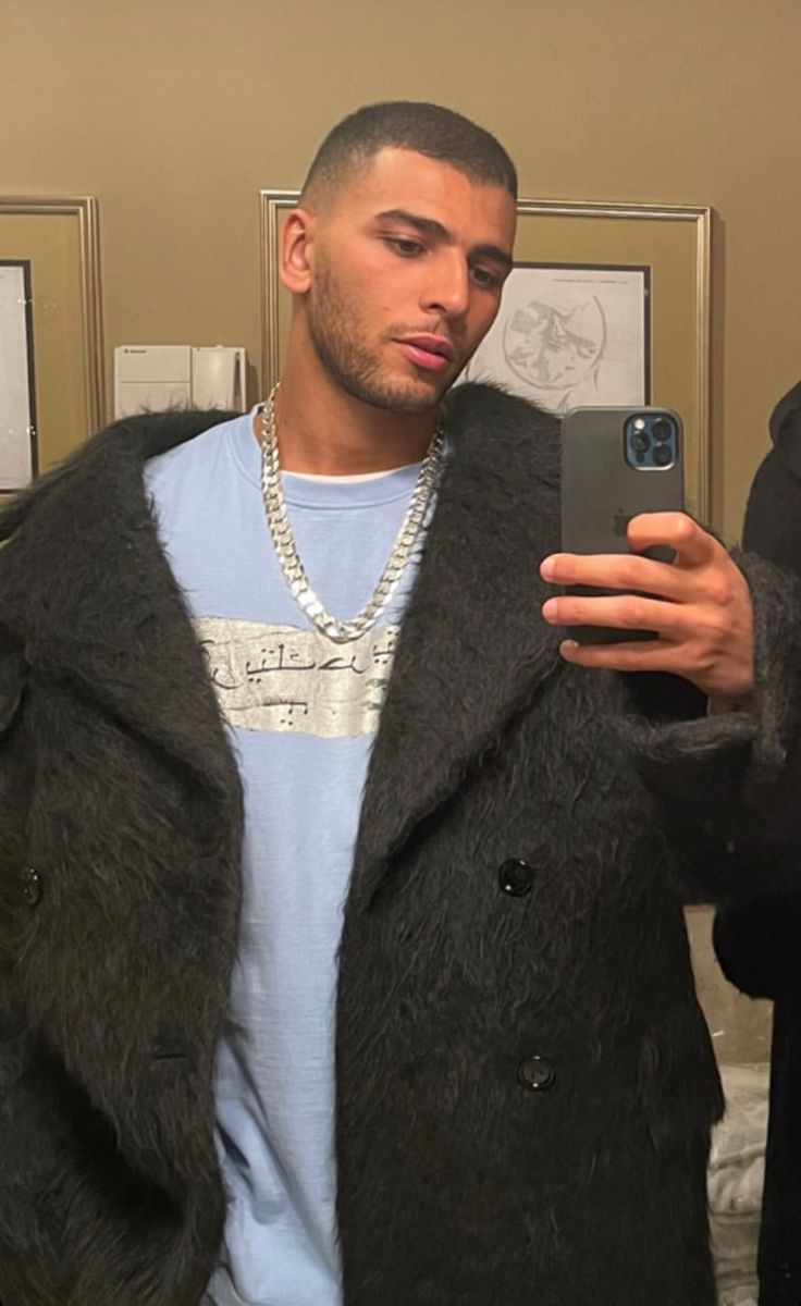 a man taking a selfie with his cell phone in front of him and wearing a fur coat