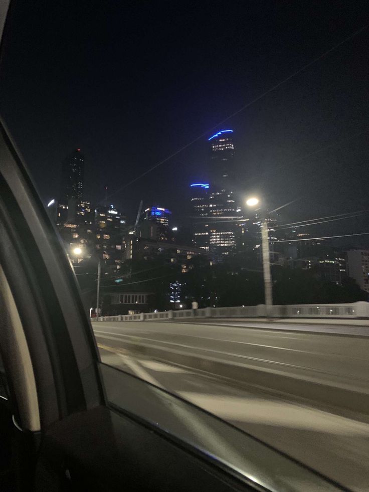 the city skyline is lit up at night as seen from inside a vehicle's windshield