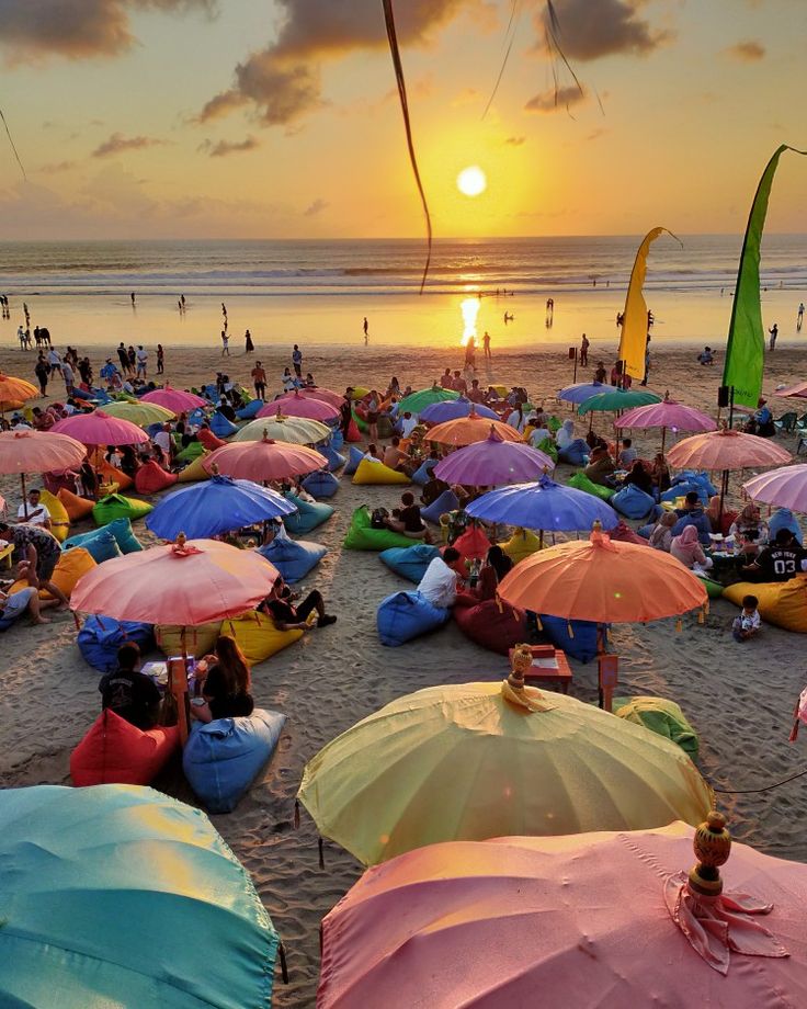 many people are sitting under umbrellas on the beach at sunset or sunrise, and one person is holding an umbrella