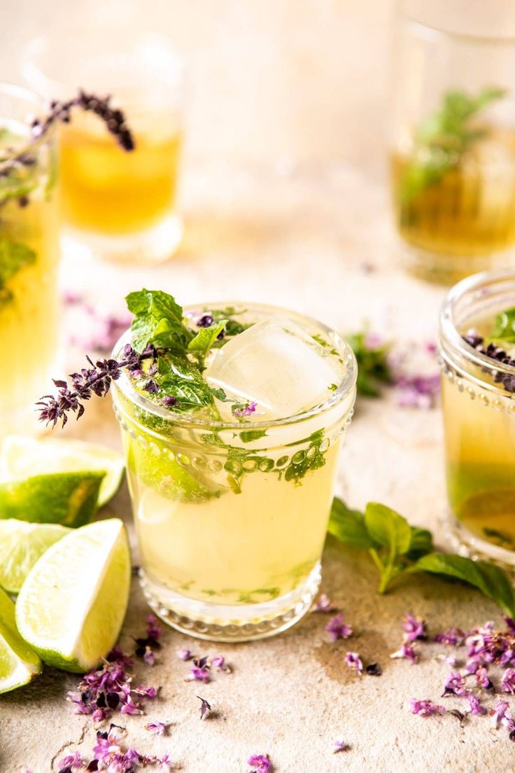 three glasses filled with lemonade and herbs next to sliced limes on a table