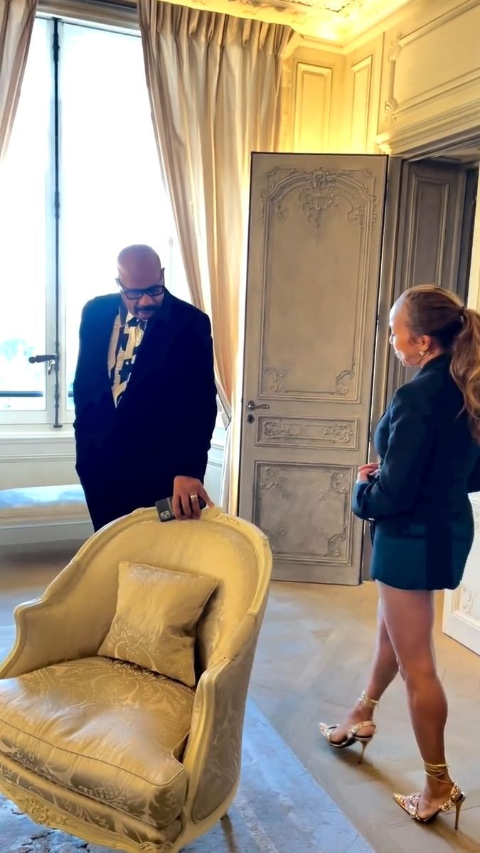 a man and woman are standing in front of a window, looking at a chair