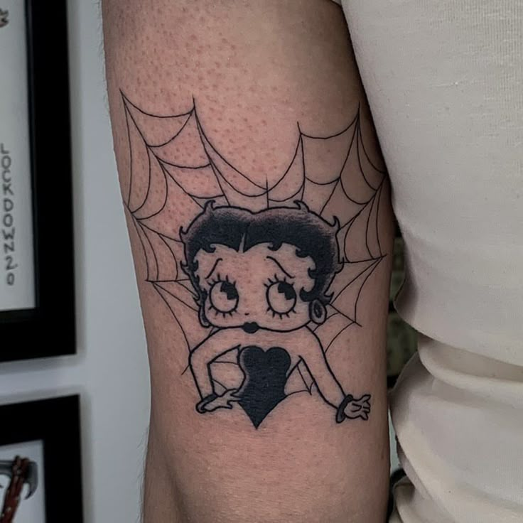 a woman's arm with a spider web tattoo on it and a cartoon character holding a heart