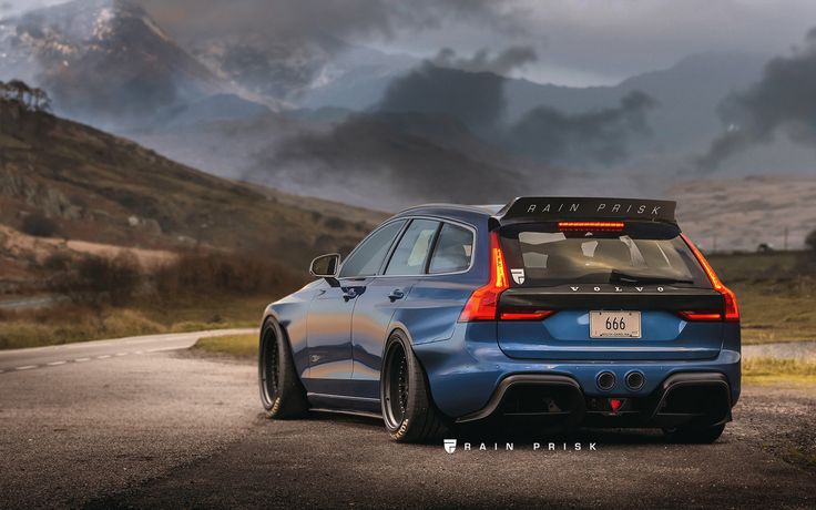 the rear end of a blue car parked on a road with mountains in the background