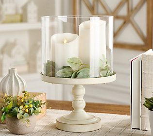 a candle holder with two candles and some plants on the table next to an open book