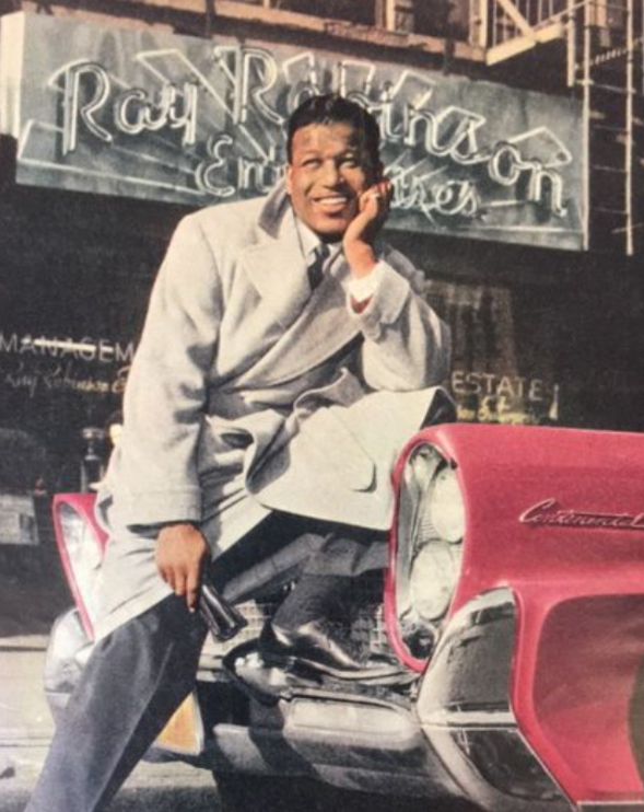 a man sitting on top of a red car talking on a cell phone