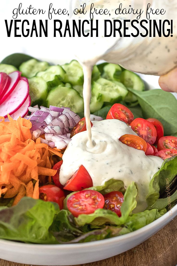 a person pouring ranch dressing on a salad with lettuce, tomatoes and cucumbers