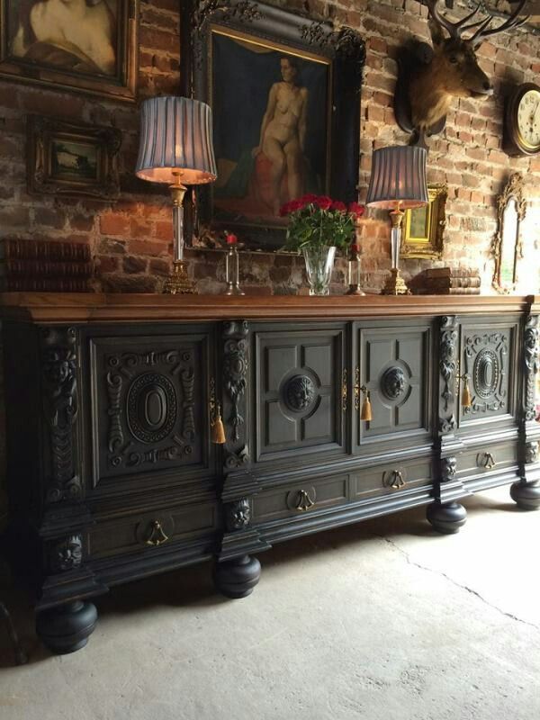 an ornately decorated sideboard in the corner of a room with brick walls and paintings on the wall