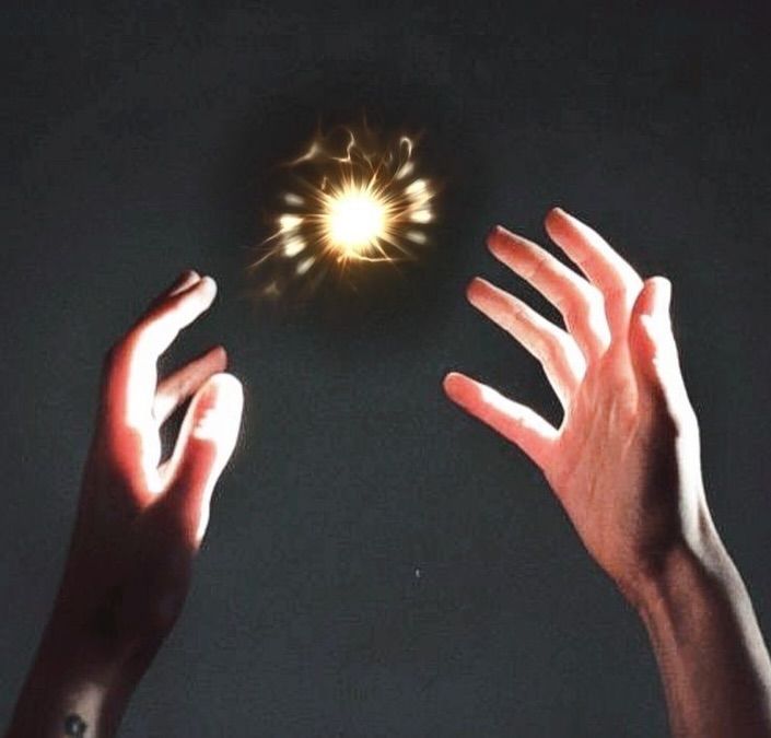 two hands reaching up towards a small object in the air with light coming from it