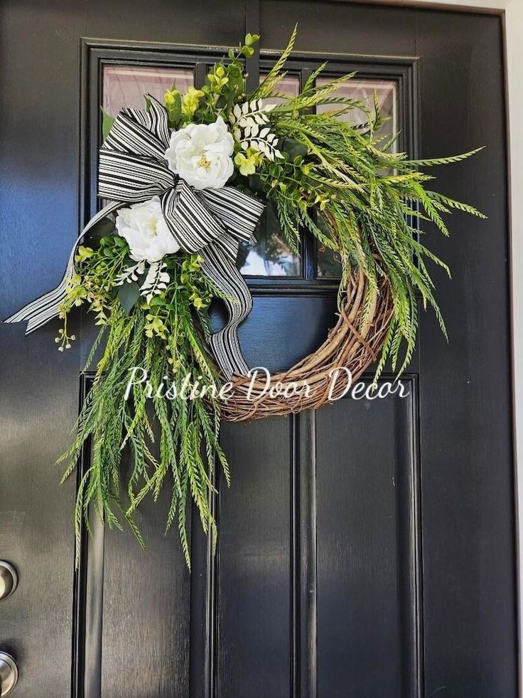 a wreath with white flowers and greenery hangs on the front door's black doors