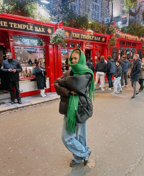 a woman with a green scarf standing in front of a red store on the street