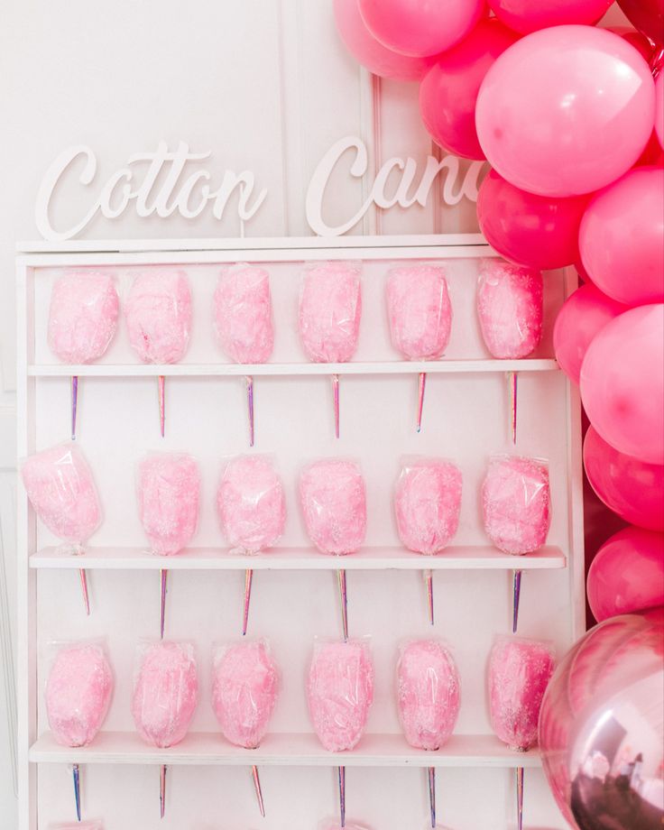 pink and white cake pops are arranged on a shelf next to the cotton candy sign