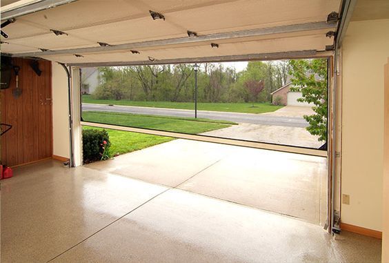 an open garage door in front of a driveway with grass and trees on the other side