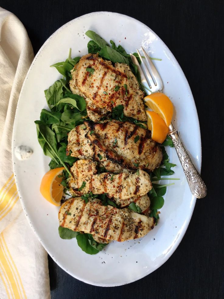 grilled chicken with spinach and orange slices on a white plate next to a fork