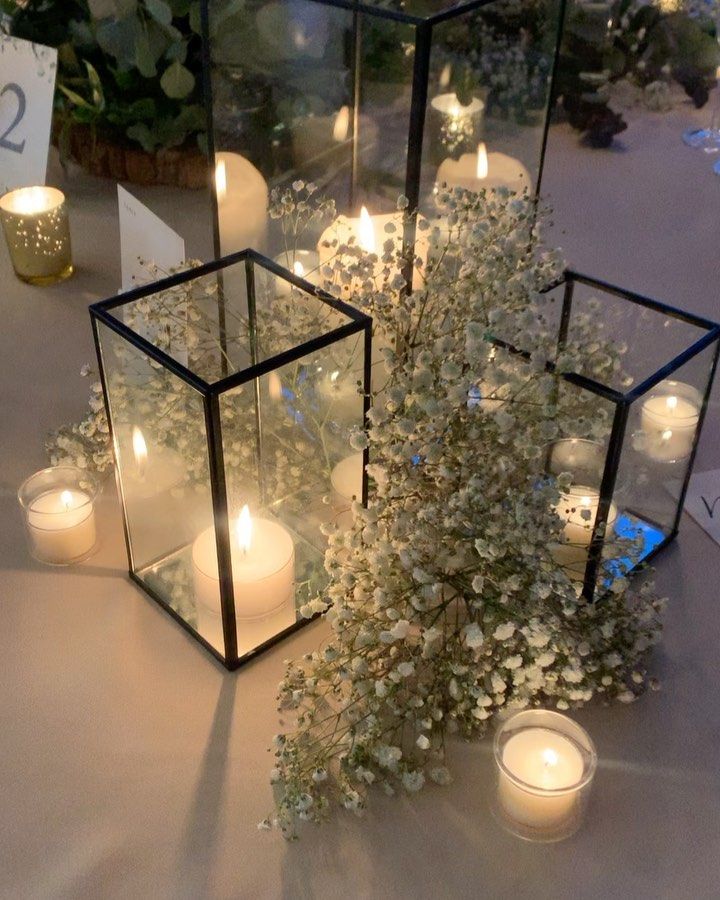 candles and flowers are arranged in glass containers on a table with white linen, which is also adorned with greenery