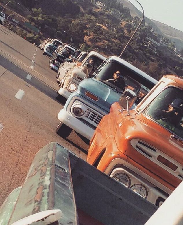 an orange truck driving down a street next to other trucks on the side of a road