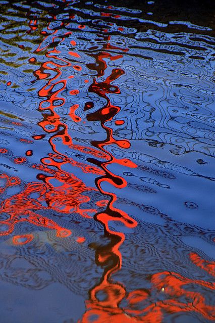 the reflection of an orange building on water with ripples in it's surface