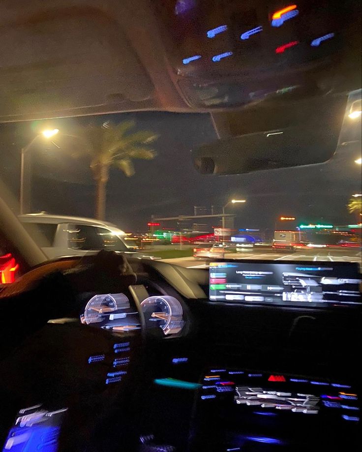 the interior of a car at night with lights on and palm trees in the background