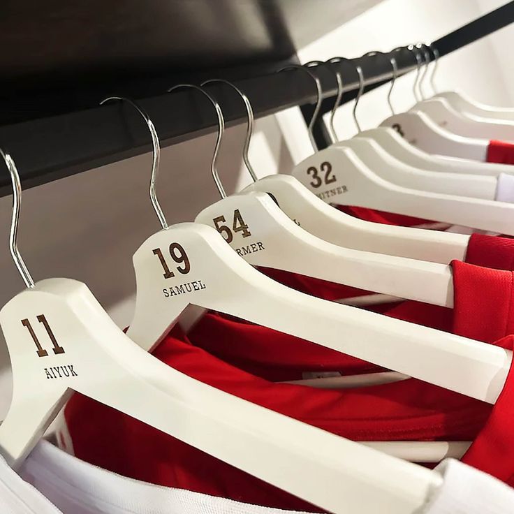 several white and red shirts hanging on black hangers in a row, with numbers printed on them