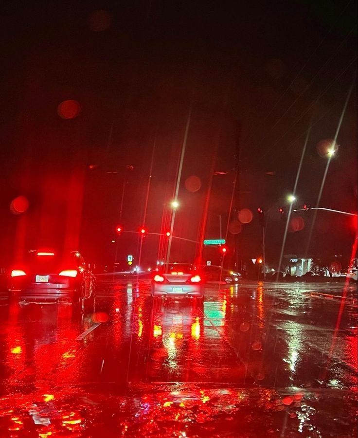 cars driving down the road at night in the rain with red lights and streetlights