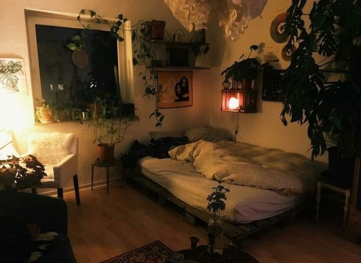 a bed sitting in the middle of a living room next to a window with plants on it