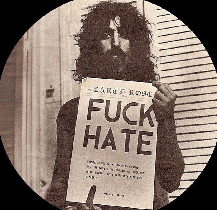 a man with long hair holding a sign that says f k hate in front of his face