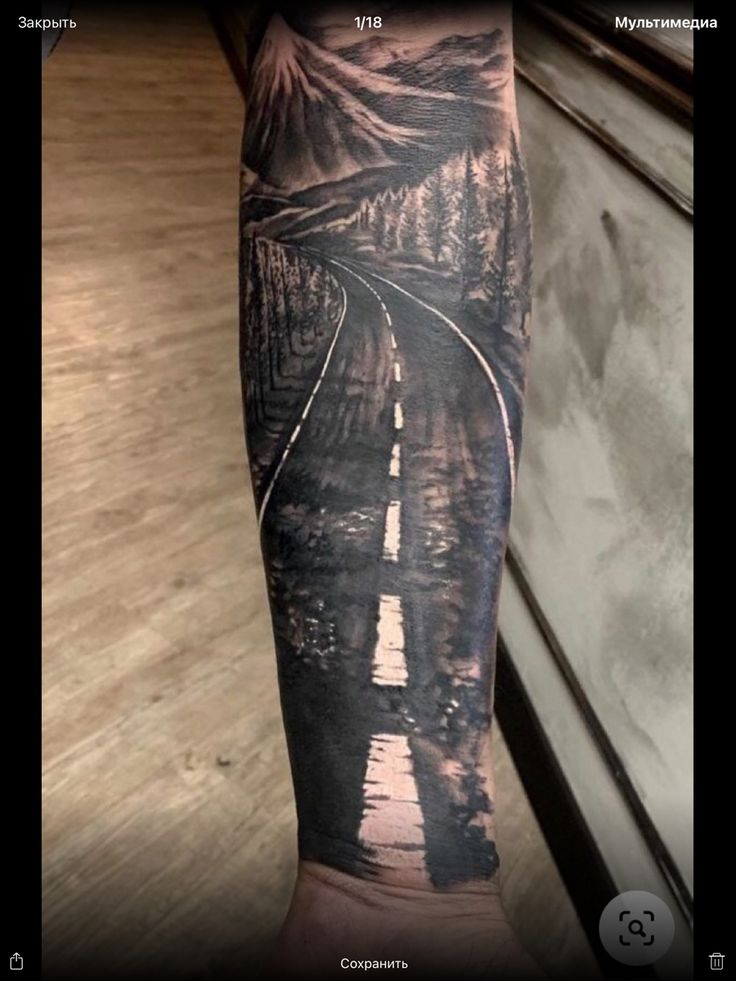 a man's arm with a train track and mountains on it