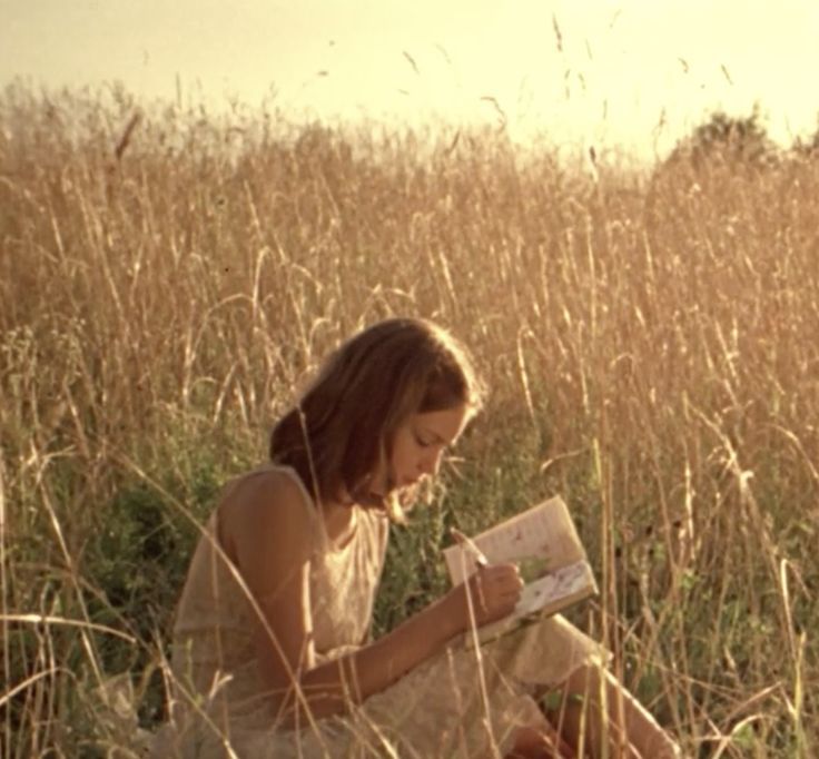 a woman sitting in tall grass reading a book